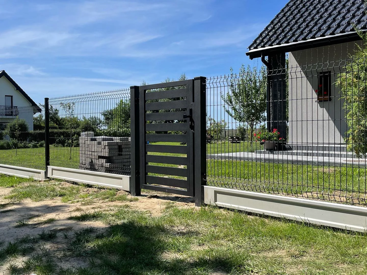 Ogrodzenie panelowe 3d z czarną metalową furtką przed nowoczesnym domem na zielonym trawniku