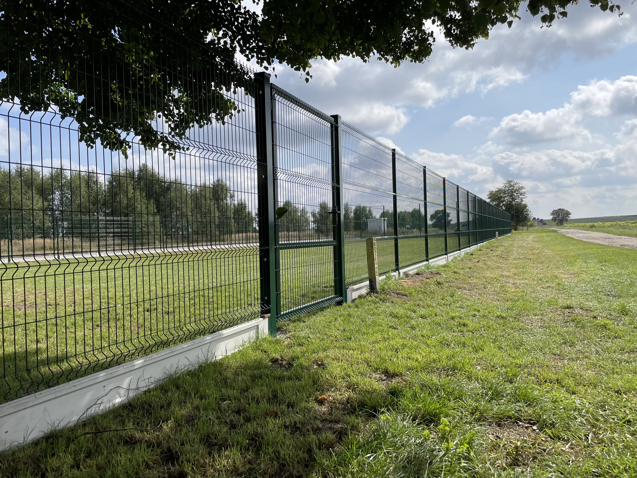 Długie zielone ogrodzenie panelowe 3D zamontowane na betonowej podmurówce w otwartym terenie