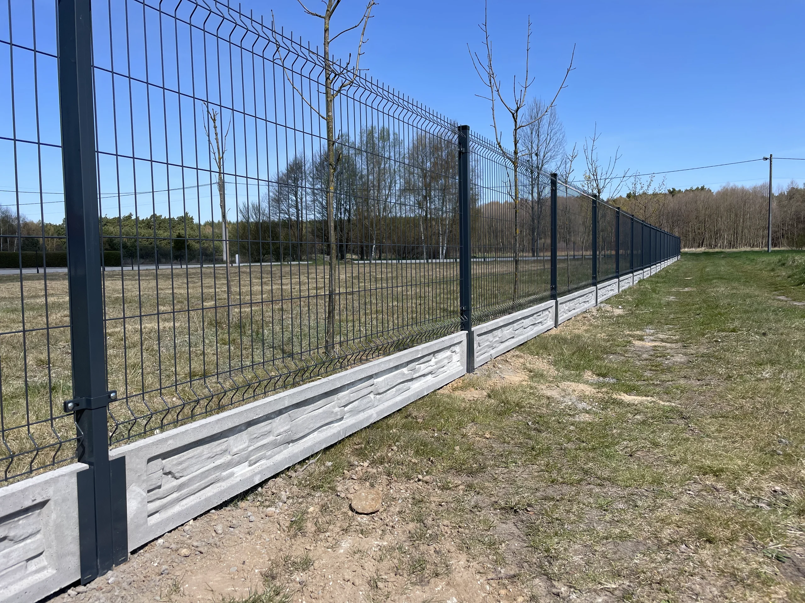 Ogrodzenia panelowe 3d z metalowych siatek na betonowym cokole osadzone na trawie przy polu