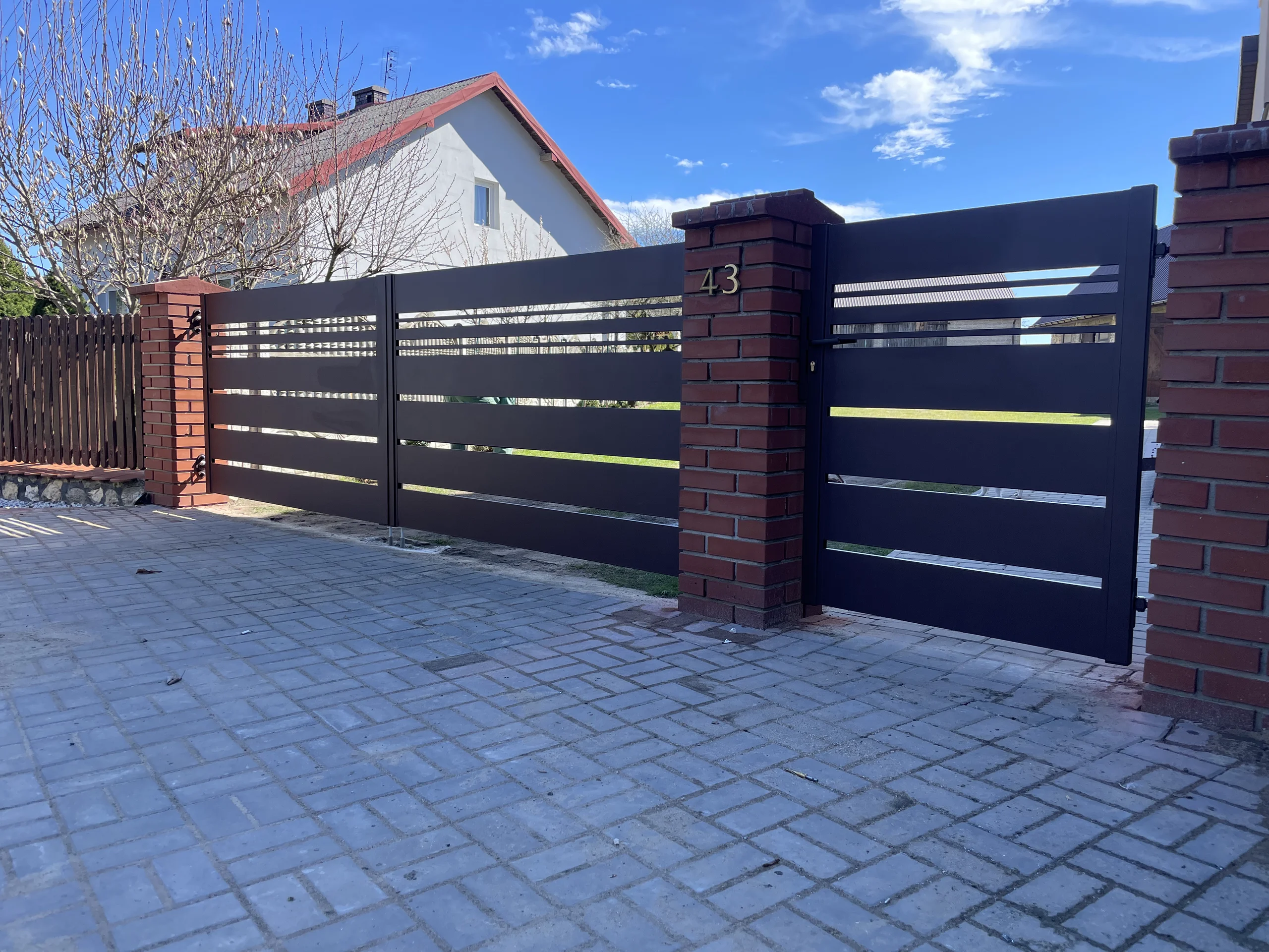 Ogrodzenie żaluzjowe z ciemnych metalowych paneli osadzone na murowanych słupkach