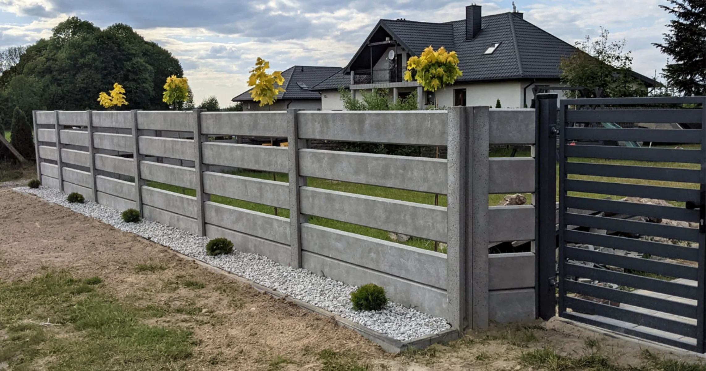 Ogrodzenia betonowe z poziomymi panelami i stalową bramą wjazdową przy nowoczesnym domu